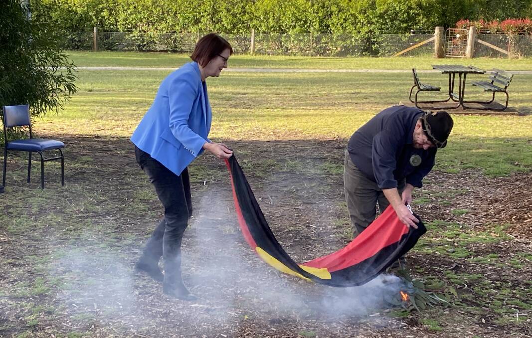 Macquarie MP Susan Templeman assists Uncle Lex during the smoking ceremony to cleanse the new flag. Picture: Supplied.