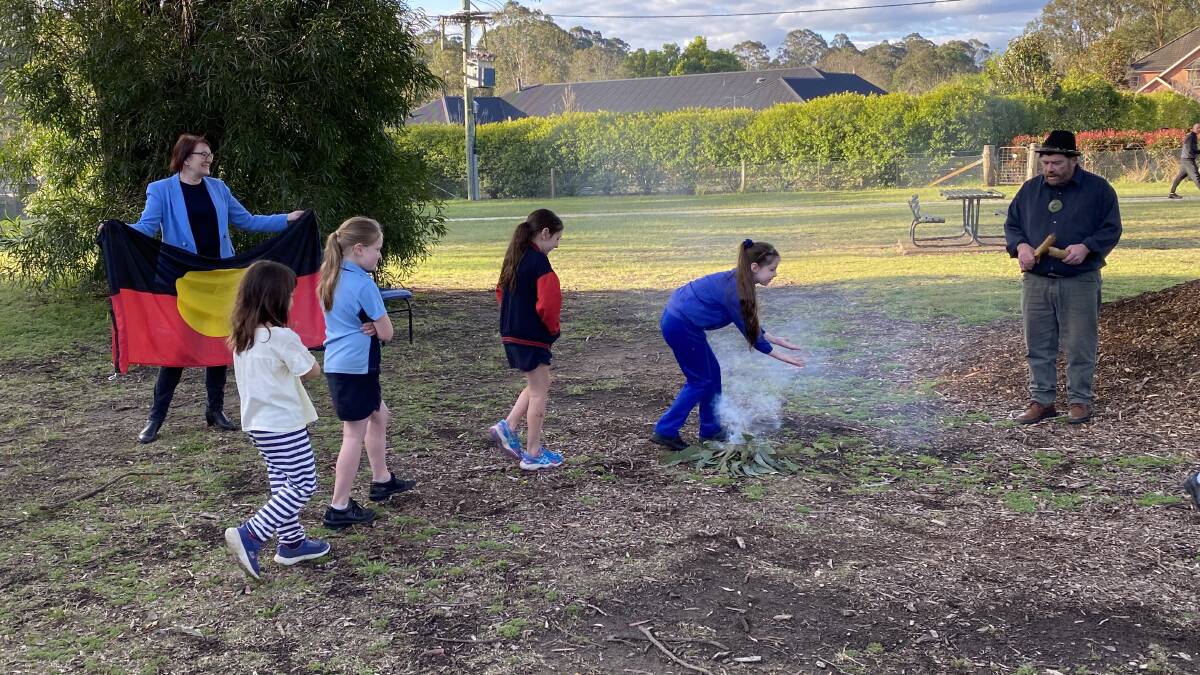 Macquarie MP Susan Templeman holds the Aboriginal flag while children from Hawkesbury Community Outreach Services take part in a smoking ceremony with Uncle Lex, who sings in language. Picture: Supplied. 