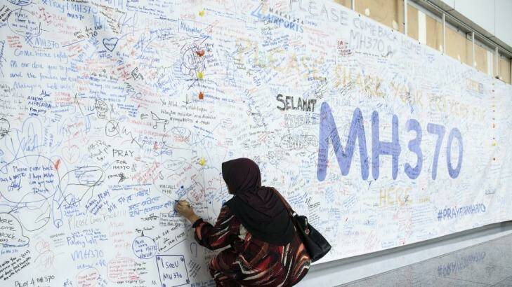 A woman writes a message on a banner for the missing airline at Kuala Lumpur International Airport. 