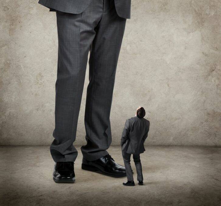 A businessman is leaning back with his hands in his pockets. He is looking up at a much larger businessman above him. There is room for text.
big and small. concept. businessman.