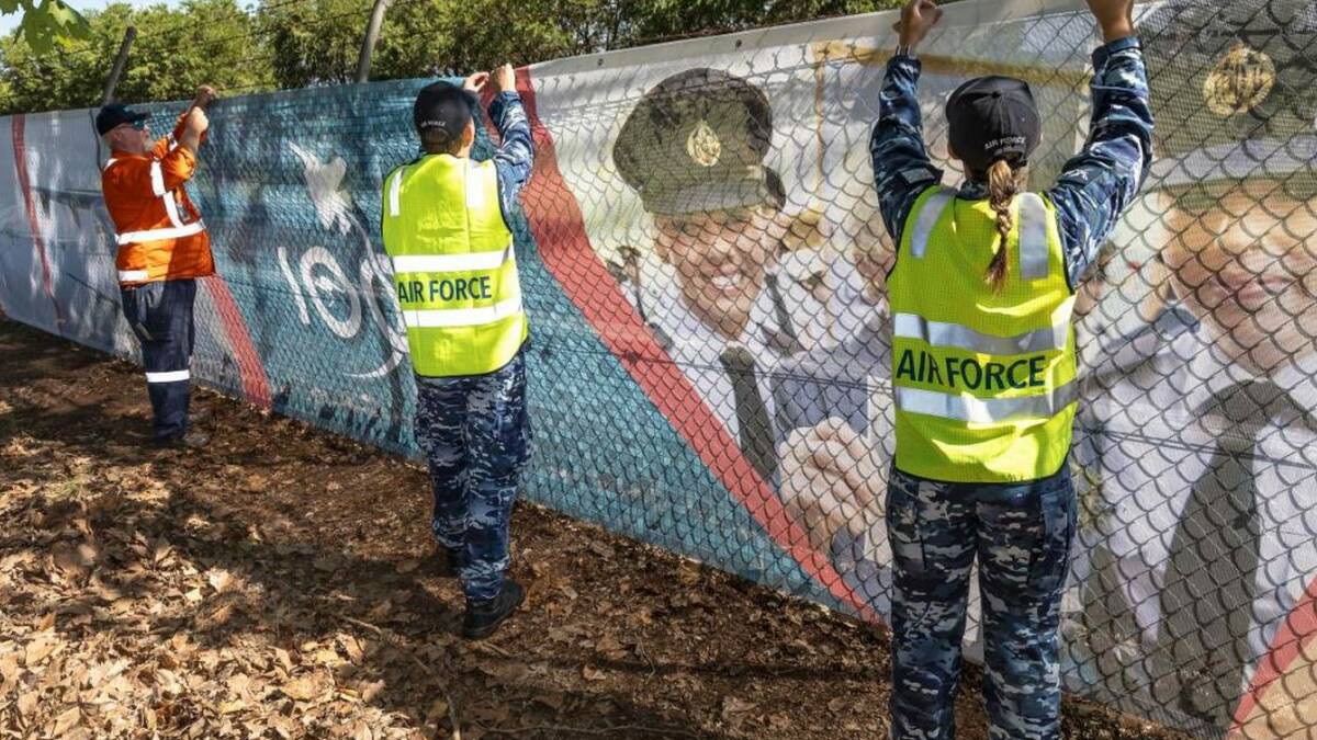 Leading Aircraftman Nathan Palmer, centre, and Aircraftwoman Alanna Hennessy both from No. 22 Squadron, assist BGIS employee Michael Gavin instal an Air Force 2021 banner on the fence at Richmond RAAF Base. Photo: Corporal Dan Pinhorn